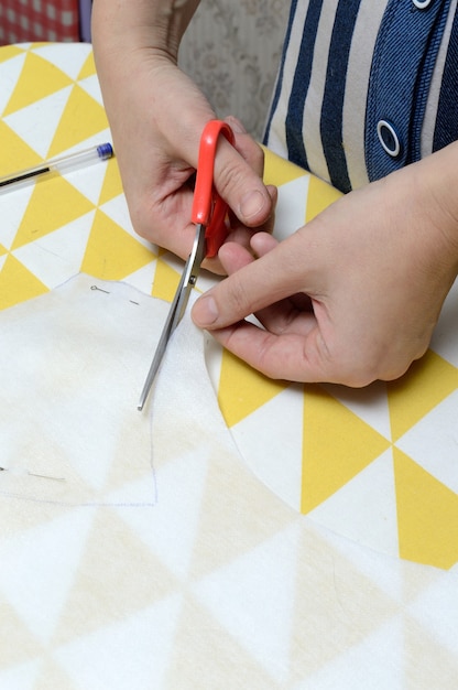 Photo women's hands cut the fabric with scissors according to the pattern on the table.