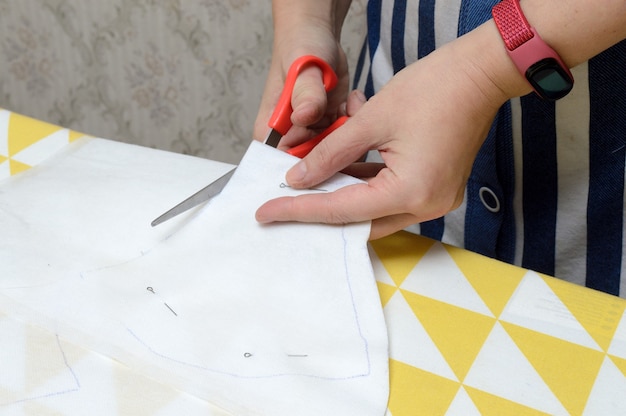 Фото Женские руки ножницами вырезают ткань по выкройке на столе.