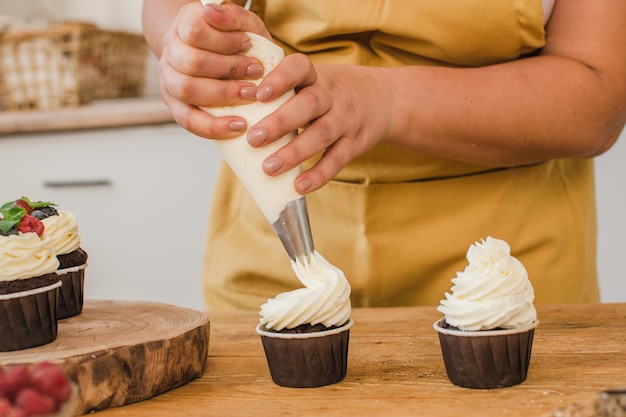 Foto le mani delle donne decorano i cupcake con la crema. concetto di professione pasticcere.