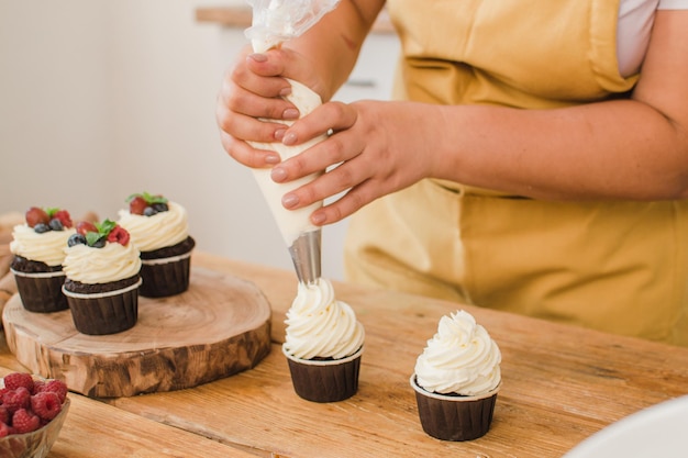 Women's hands decorate cupcakes with cream. Pastry chef profession concept.