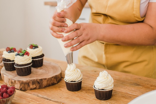 Le mani delle donne decorano i cupcake con la crema. concetto di professione pasticcere.