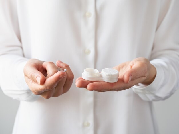 Women's hands hold a contact lens on their finger and a container for contact lenses.