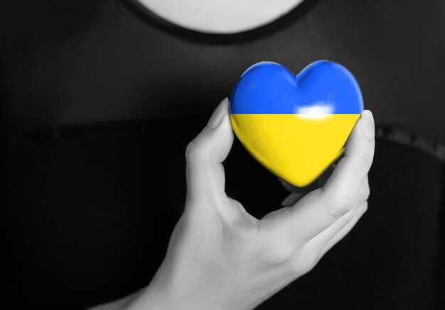 Women's hands hold a heart in the colors of the Ukrainian flag pray for Ukraine Stand with Ukraine