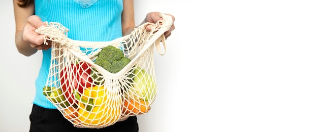 Women's hands hold a mesh bag with vegetables on a white background