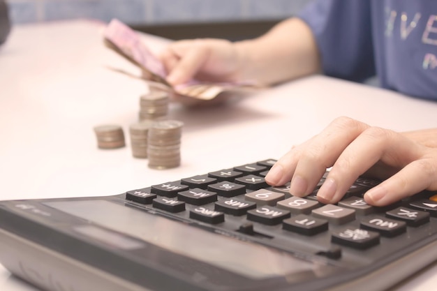 Foto le mani delle donne tengono i soldi e utilizzano la calcolatrice con una pila di monete e calcolatrice concetto di risparmio di denaro e concetto di investimento