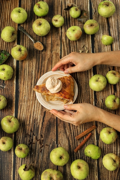 Women's hands hold a plate with a piece of homemade apple pie and a ball of ice cream on a table