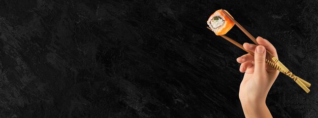 Women's hands hold sushi rolls with sticks. Black background. Creative concept.