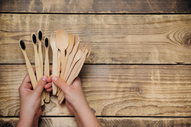 Women\'s hands hold wooden bamboo spoons, knives, forks and\
toothbrushes. the concept of zero waste without plastic.