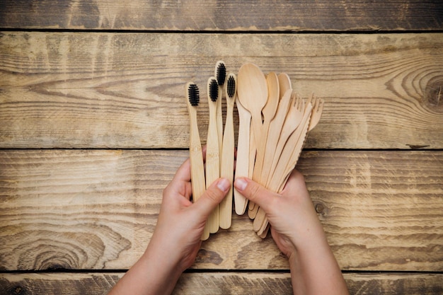 Le mani delle donne tengono cucchiai di legno di bambù, coltelli, forchette e spazzolini da denti. il concetto di zero rifiuti senza plastica.