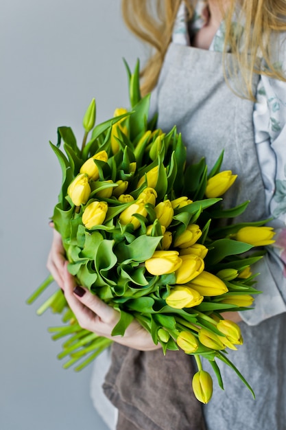 Women's hands holding an armful of yellow tulips. 