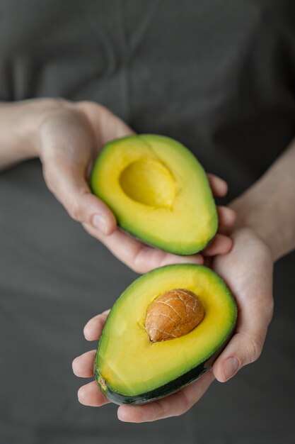 Women's hands holding avocado, Caucasian woman in dark t-shirt, kitchen, cooking chef, ripe and delicious avocado, healthy and healthy food, raw fruits and vegetables vegan vegetarian