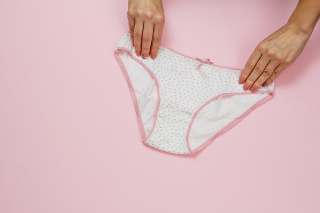 Women's hands holding beautiful cotton white panties on pink background. Woman underwear set. Top view.