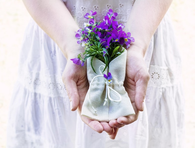 Женские руки держат букет цветов анютиных глазок в текстильном конверте Нежность и красота Выборочный фокус