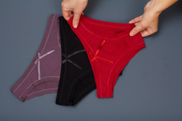 Women's hands holding red cotton panties on gray background. Woman underwear set. Top view.