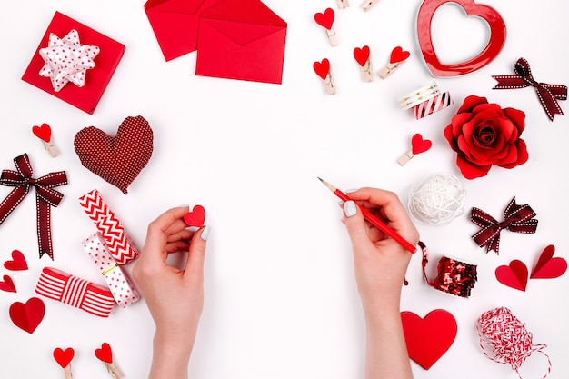 Women's hands holding valentine card on white background with romantic decoration. flat lay