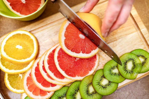 Фото Женские руки домохозяйки режут ножом свежий грейпфрут на разделочной доске кухонного стола
