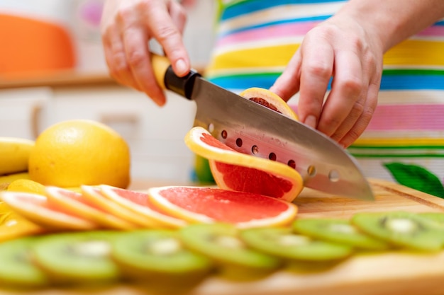 女性の手主婦は台所のテーブルのまな板の上でナイフで新鮮なグレープフルーツを切りました
