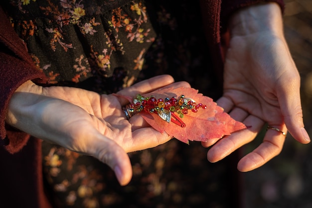 In women's hands is an autumn leaf of autumn and a hair accessory made of glass beads.