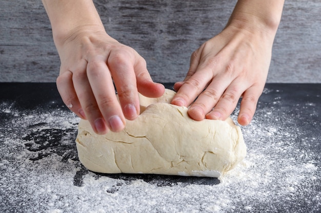 Women's hands knead the dough on a wooden table.