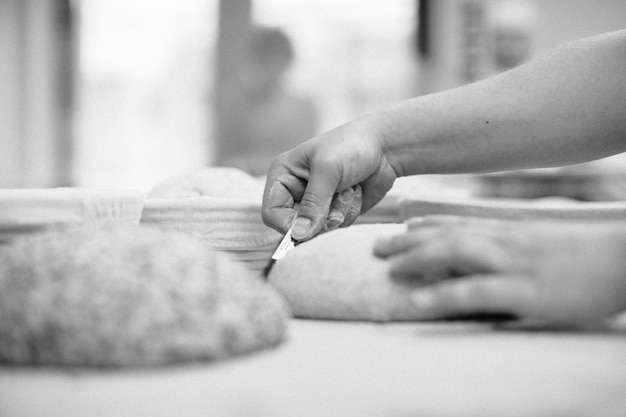 Women's hands make an incision on a round dough before baking breadxA