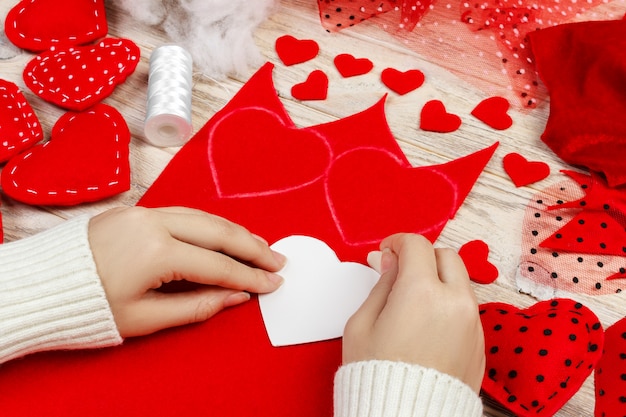 Women's hands make red hearts from the fabric. Preparation for St. Valentine's Day. homemade festive decorations. Above view, flat lay