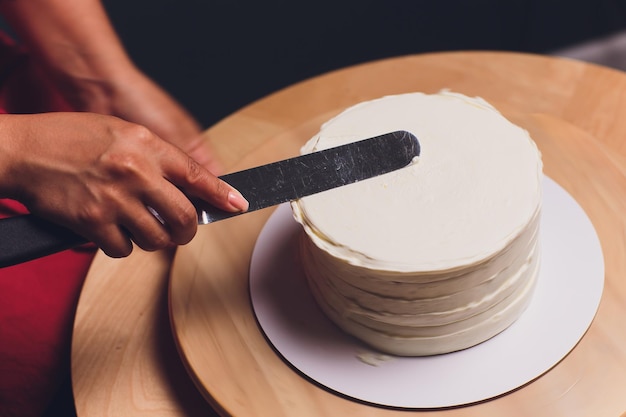 Photo women's hands making biscuit cake with white cream using a cooking spatula