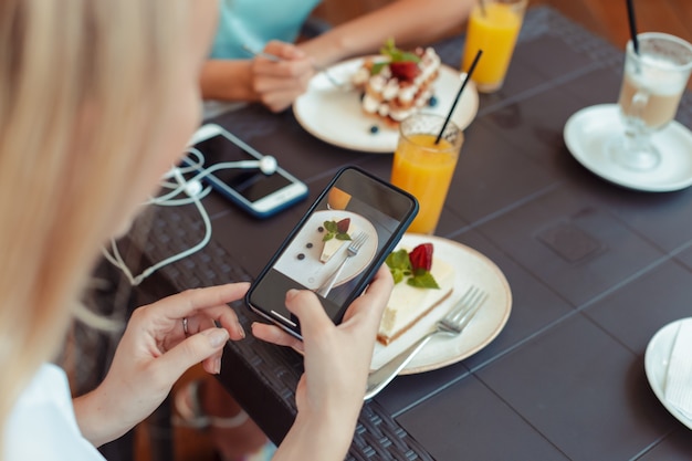 Le mani delle donne che fanno la foto di un dolce dessert sul telefono cellulare mentre sono seduti in un comodo ristorante