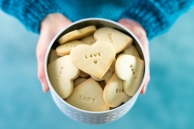 Women's hands offer a heart shaped cookie box with LOVE letters