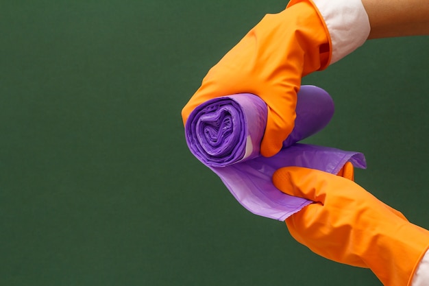 Женские руки в оранжевой защитной перчатке с мешками для мусора на зеленом фоне. Концепция стирки и очистки.