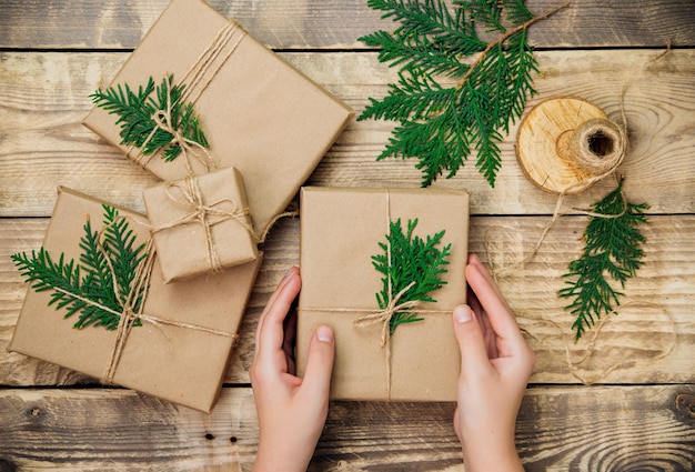 Women's hands pack boxes in kraft paper on a wooden background. Delivery service.Environmentally friendly material. Handmade art craft. The concept of Christmas and New Year.