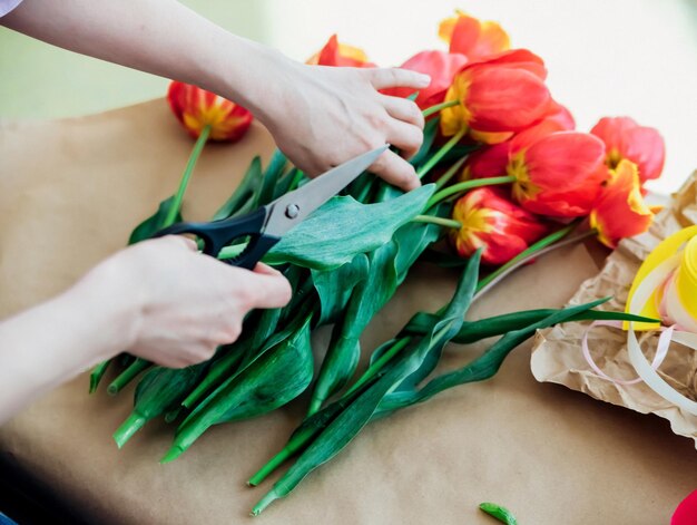 Women's hands pack a festive bouquet in wrapping paper The florist makes an assembly with red tulips in the workshop A woman at work small business or hobby