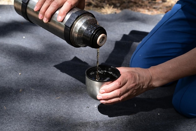 Le mani delle donne versano il tè da un thermos nella foresta durante un picnic