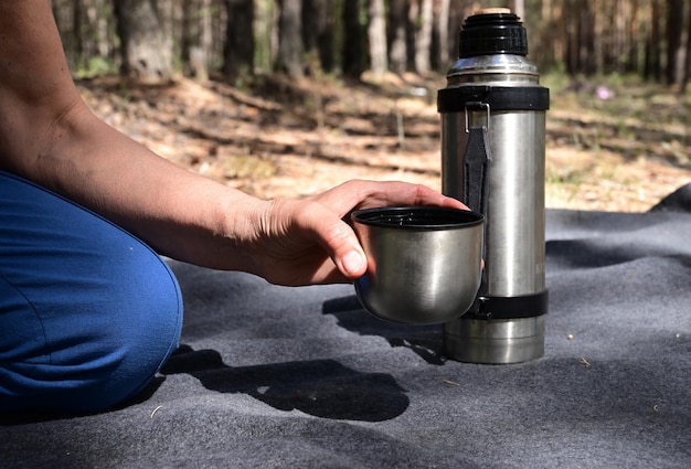 Women's hands pour tea from a thermos in the forest on a picnic