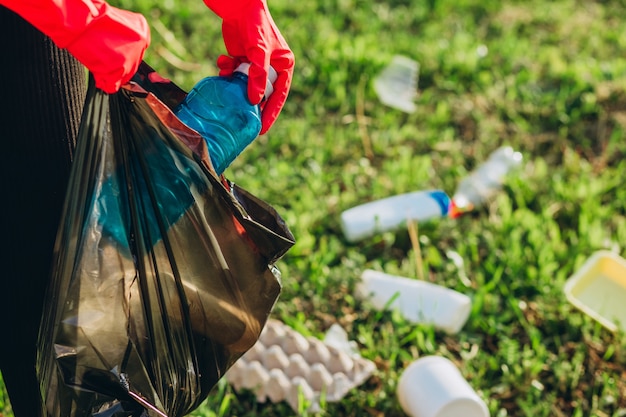 Foto mani da donna in guanti di gomma rossa. la donna raccoglie la spazzatura nella borsa. immondizia volontaria di scavenge nel parco di estate. bella donna progressista che fa uno sforzo per aiutare l'ambiente