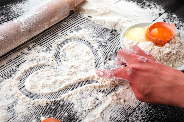 Women's hands roll out the dough on a black table sprinkled with flour.