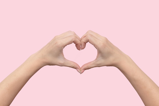 Женские руки показывают знак сердца пальцами на розовом фоне