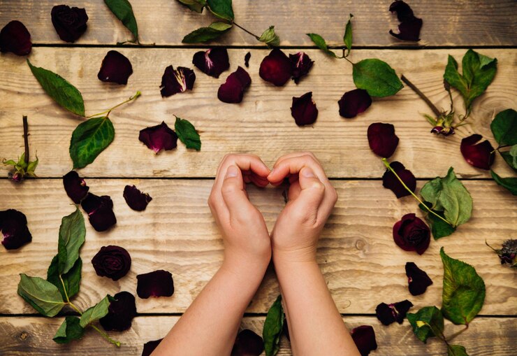 Photo women's hands show the shape of a heart. dry rose petals on a wooden background. herbarium and dried flowers. aromatherapy. texture and background.