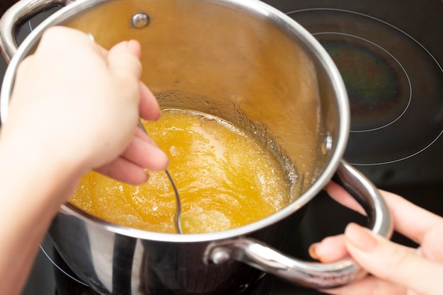 Women's hands stir honey on the stove