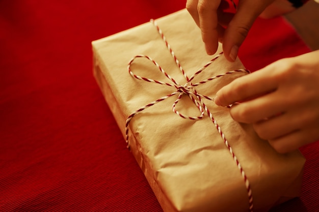 Женские руки завязывают ленточку на подарке на красном фоне