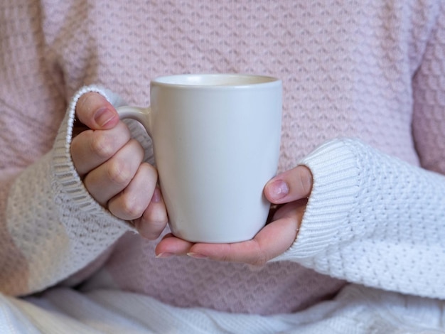 Women's hands in a warm knitted sweater with a white mug of cappuccino