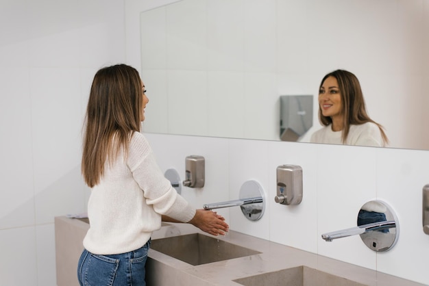 ミクサーからの水噴射の下の女性の手中年女性がトイレで手を洗っています