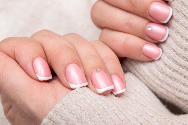 Mani delle donne con french manicure e strass su unghie rettangolari sullo sfondo di un maglione