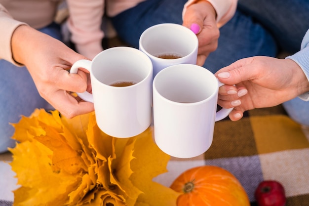 Photo women's hands with white mugs at a picnic. friends drink hot tea at a picnic in autumn, close-up view from above. selective focus