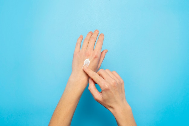 Фото Женские руки. женщина смазывает крем на руке на синем. концепция косметики, ухода за кожей, лосьон, макияж, спа.