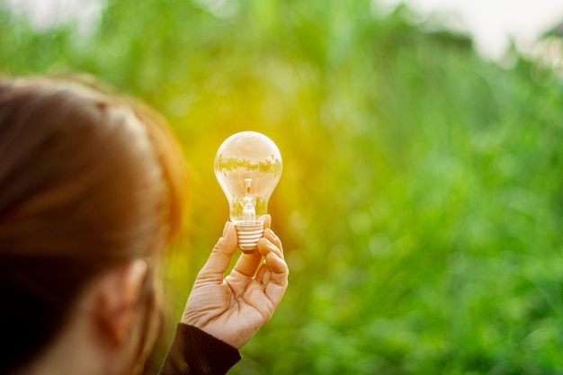 Women's is holding sparking light bulb against nature on green leaf. - New idea and innovation concept.