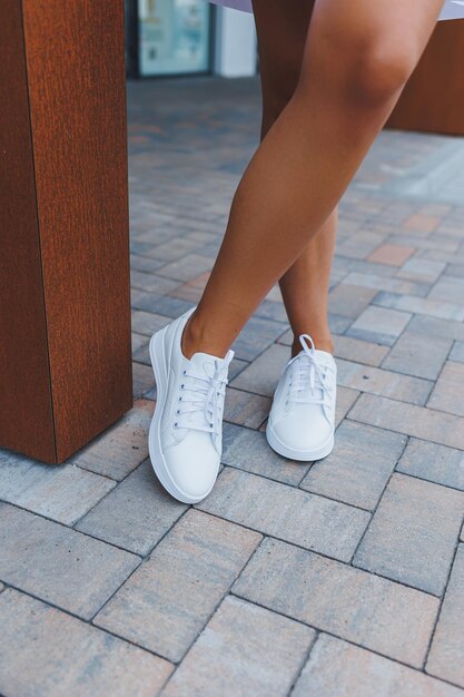 Women's legs closeup in white leather sneakers made from natural leatherCollection of women's summer shoes