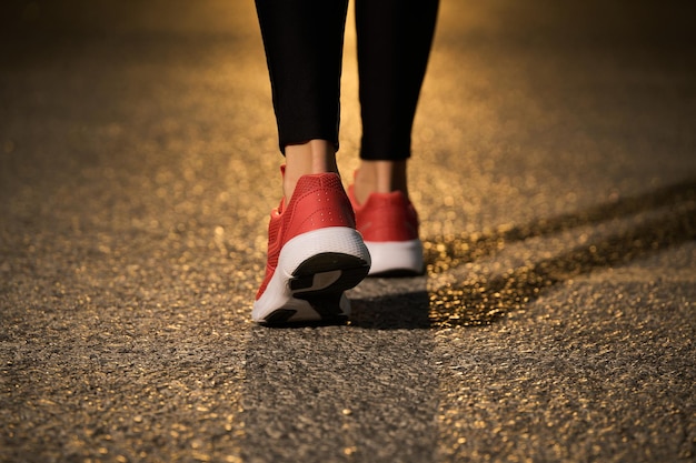 Women's legs and feet walking in sneakers on asphalt in sunset sunshine