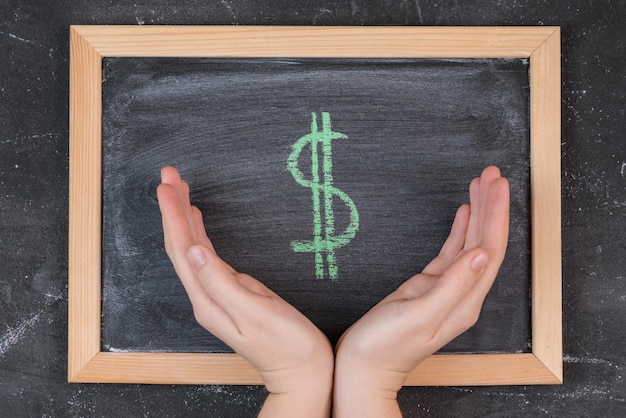 Photo women's palms gently embrace the green dollar symbol on the blackboard top view