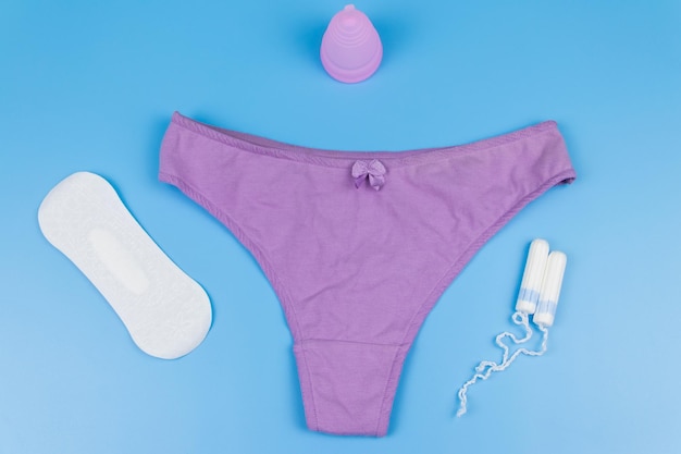 Women's panties with menstrual cups sanitary pads and tampons on pastel blue background Top view Concept of critical days menstruation feminine hygiene