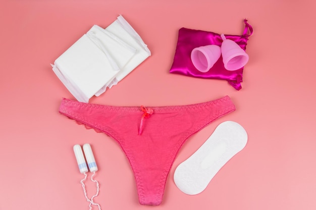 Women's panties with menstrual cups sanitary pads and tampons on pastel pink background Top view Concept of critical days menstruation feminine hygiene